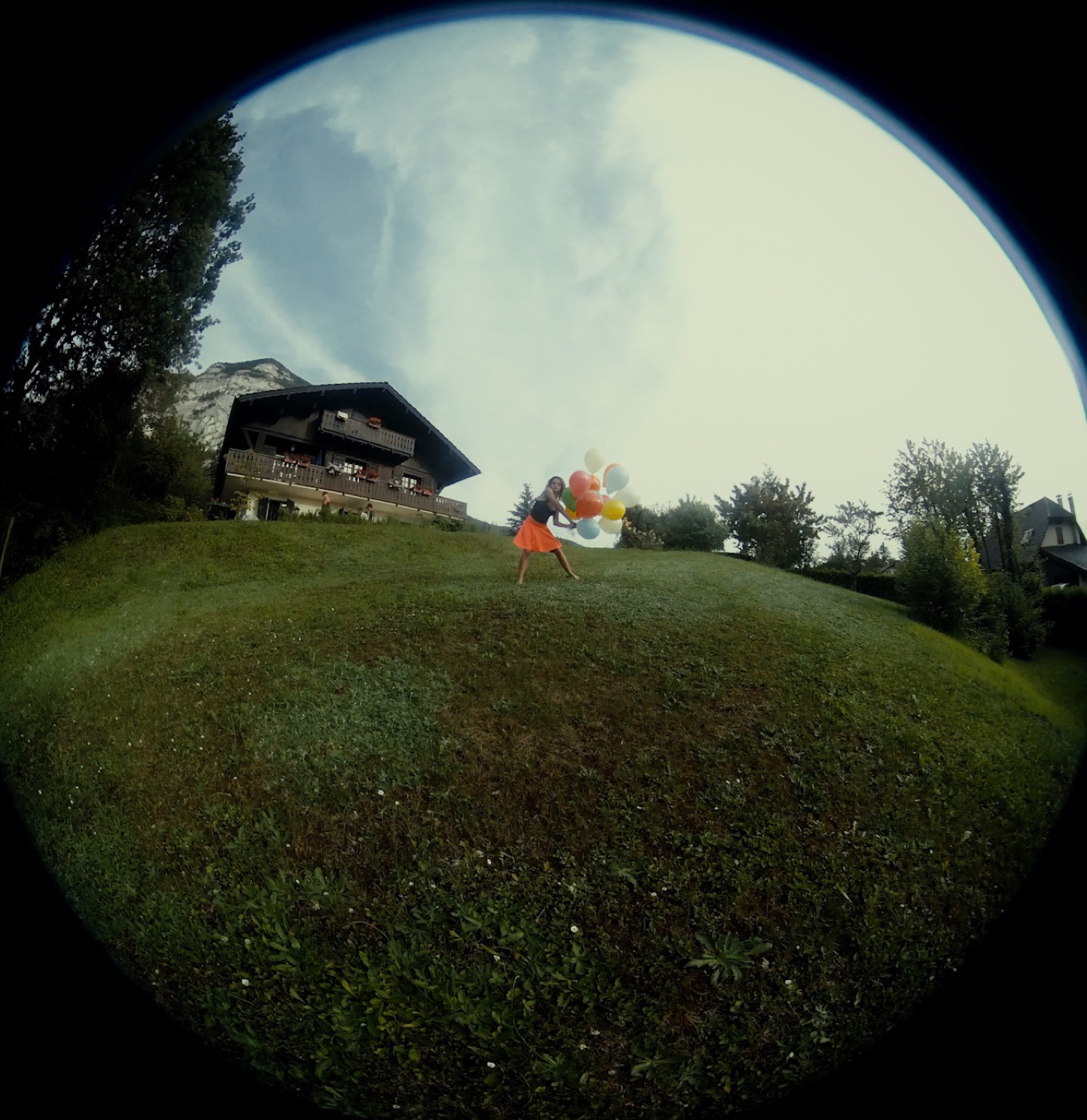 TERRAIN still: dancer with balloons in front of a Swiss chalet